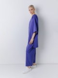 Vista laterale della maxi blusa in tessuto di neoprene ultralight con scollo rotondo a barchetta, e maniche a kimono lunghe al gomito. Corpo molto ampio. Lunghezza asimmetrica con spacchi laterali.