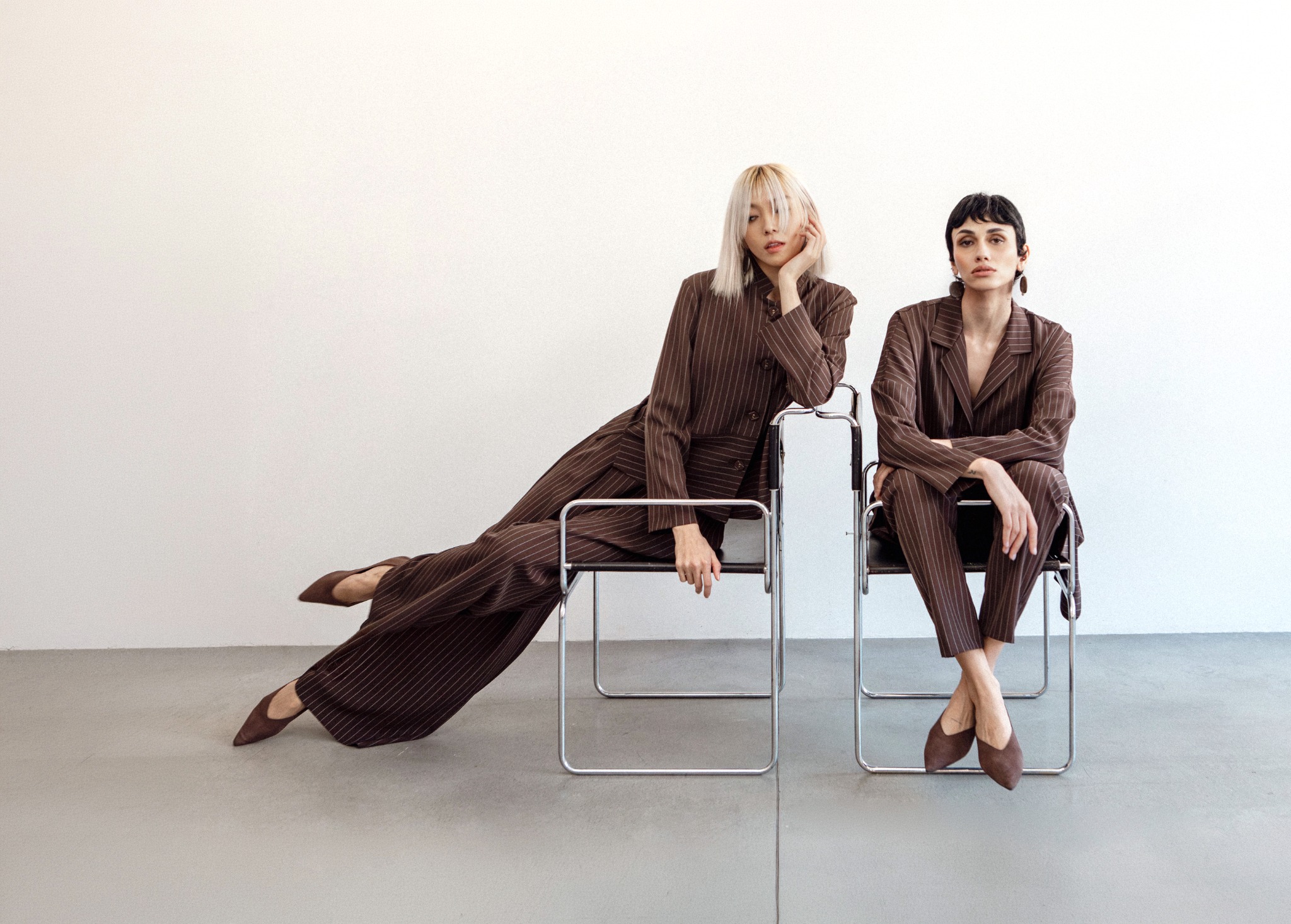Two models in brown pinstriped suits sitting on chrome chairs